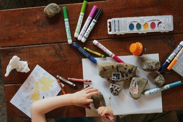 a child decorates some rocks with stickers and paints