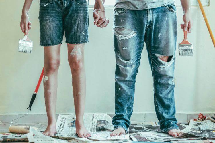 A How-To couple with paintbrushes standing on newspapers
