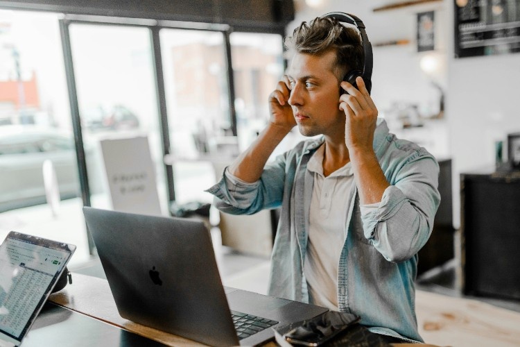 A man standing at a computer and adjusting his headphones