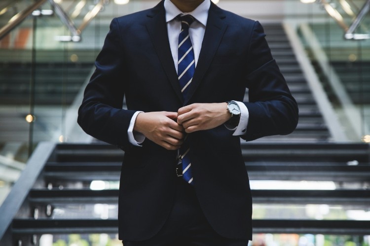 a man with a nice suit and watch standing in front of some stairs