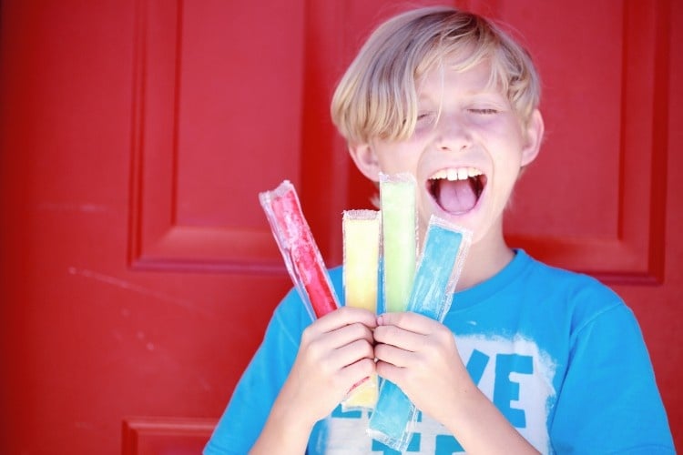 A smiling boy holding four popsicles