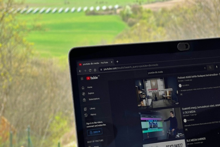 a view of a laptop displaying a youtube page with a field behind the laptop