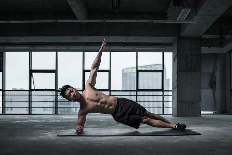 Asian fitness guy doing a side plank in a factory gym