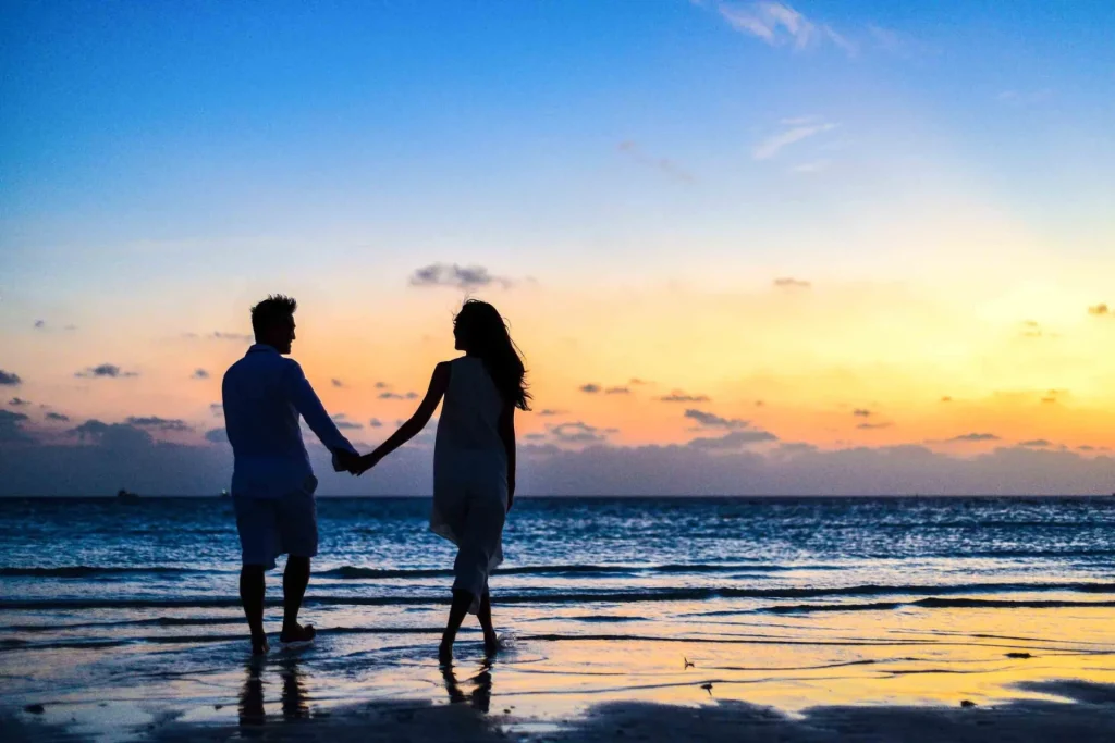 Couple holding hands walking on the beach at sunset
