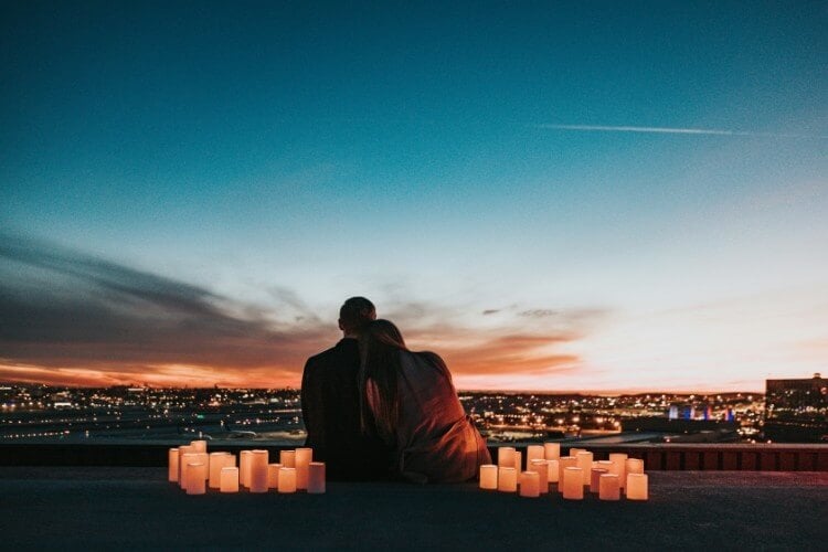 couple sits with nice city view surrounded by candles. 