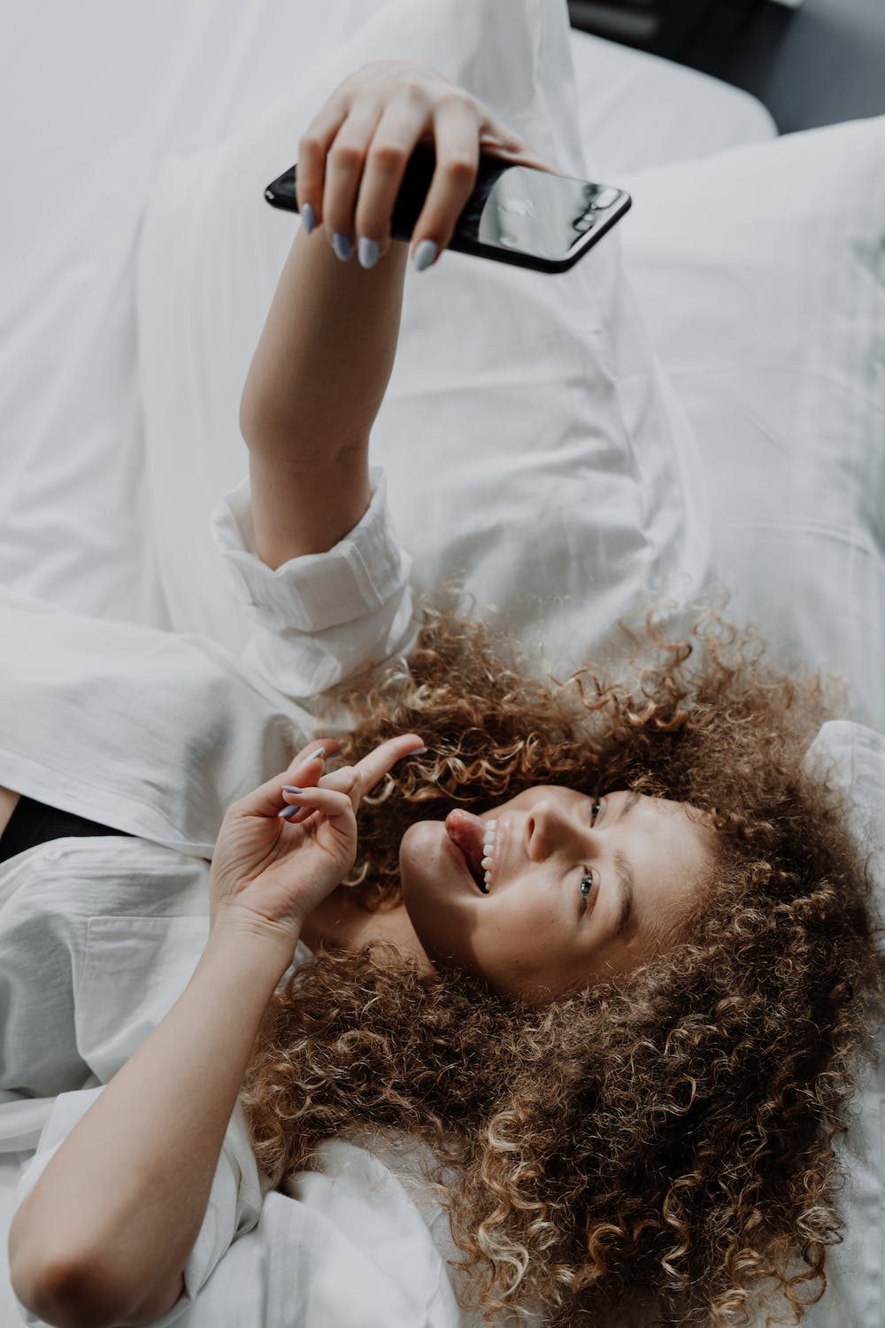 Curly haired girl taking a selfie while lying on her bed