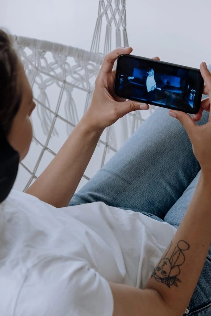 A woman laying in a hammock watching Youtube on her phone