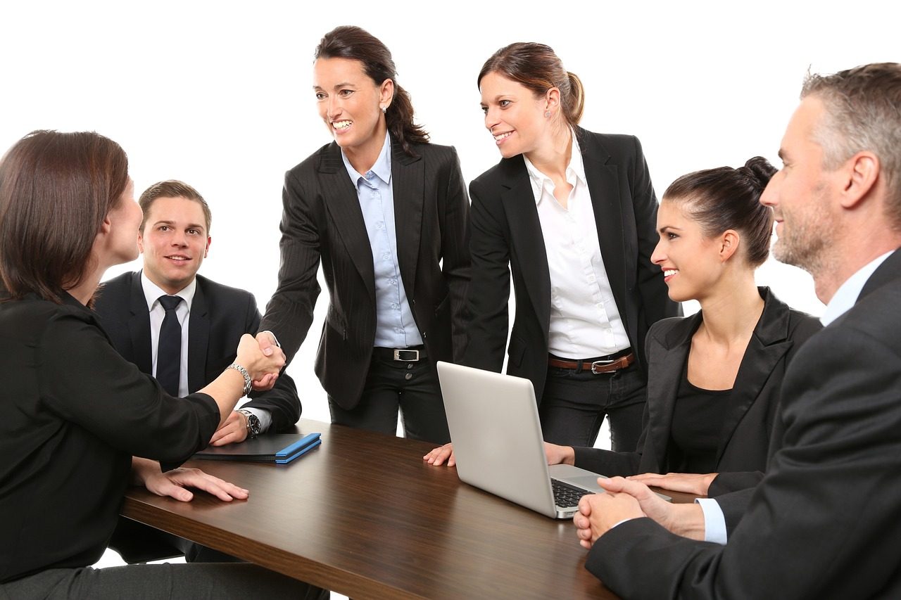 men and women in black suits around a large table conducting business