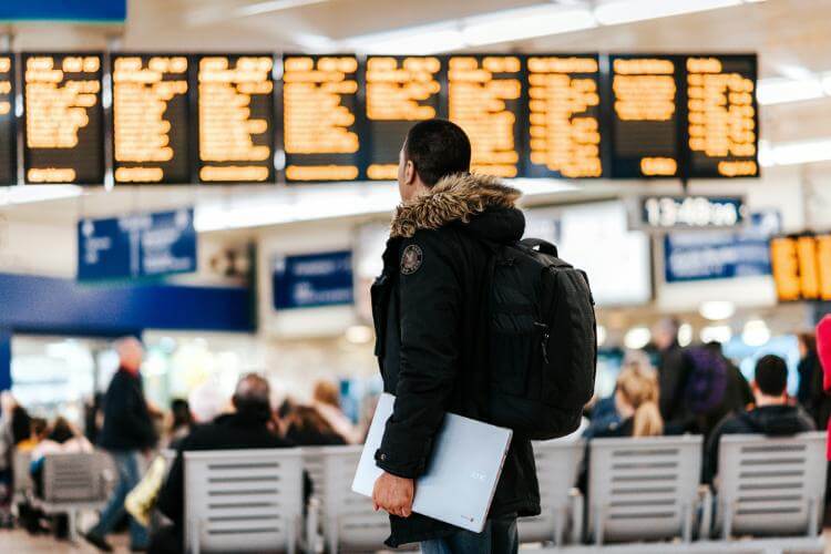 Man holds laptop in airport terminal.