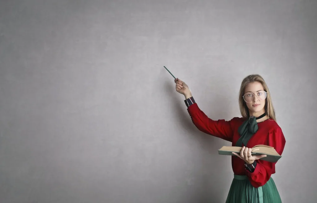 Teacher in a red dress with a book in front of a wall